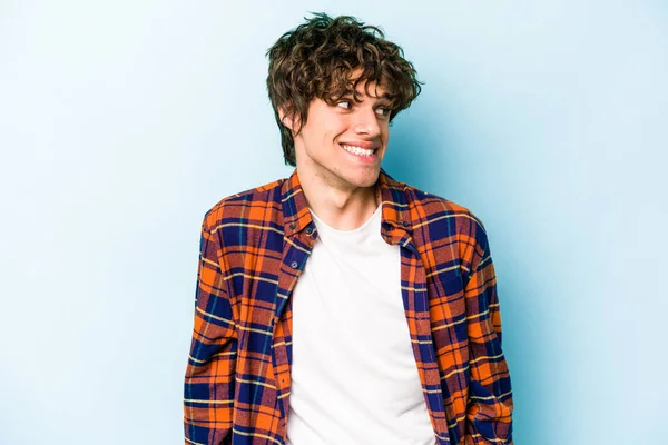 Mavi arka planda izole edilmiş genç beyaz adam gülüyor ve gözlerini kapıyor, rahatlamış ve mutlu hissediyor..