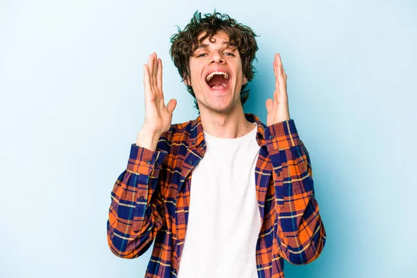 Mavi arka planda izole olmuş genç beyaz adam yüksek sesle gülüyor ve elini göğsüne koyuyor..