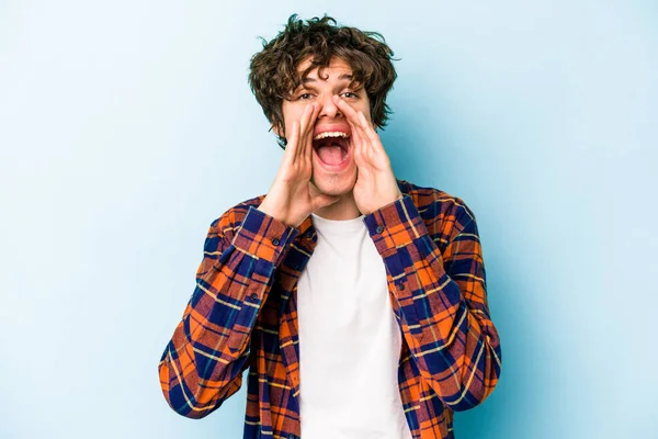 Kafkasyalı genç adam mavi arka planda izole edilmiş. Dedikodu yapıyor, bir şeyleri bildiriyor..