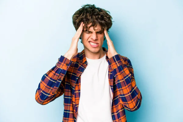 Genç beyaz adam mavi arka planda izole edilmiş tapınaklara dokunuyor ve başı ağrıyor..