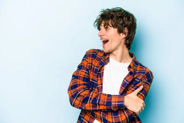 Mavi arka planda izole edilmiş genç beyaz adam kollarını kavuşturarak gülümsüyor..