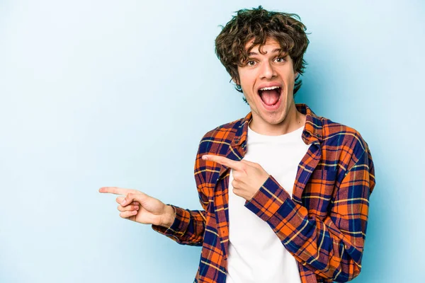 Kafkasyalı genç adam mavi arka planda izole edilmiş. İşaret parmağıyla işaret ettiği için heyecanlı..