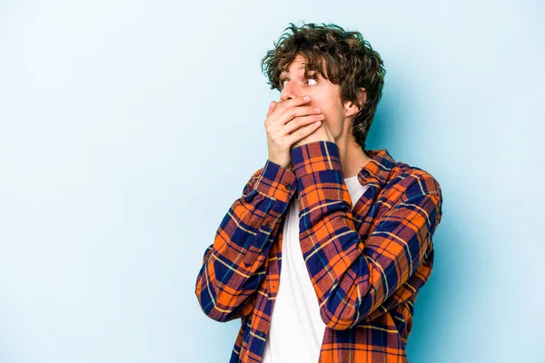 Kafkasyalı genç adam mavi arka planda izole edilmiş. Düşünceli bir şekilde ağzıyla ağzını kapatan bir fotokopi odasına bakıyor..