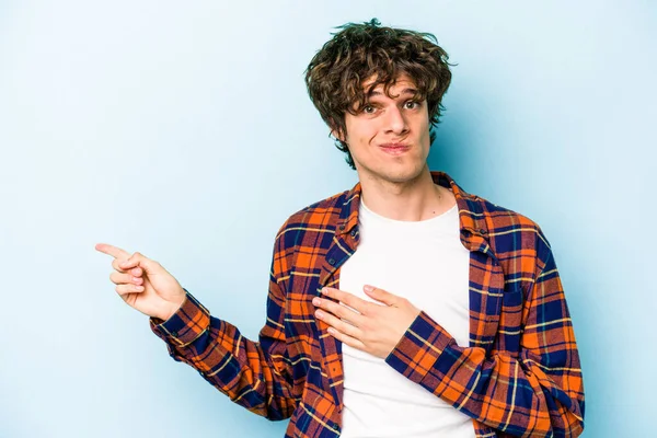 Mavi arka planda izole edilmiş genç beyaz adam işaret parmağıyla fotokopi alanını işaret ederek şok oldu..