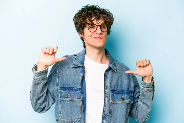 Mavi arka planda izole edilmiş genç beyaz adam gururlu ve kendinden emin hissediyor, örnek olarak.