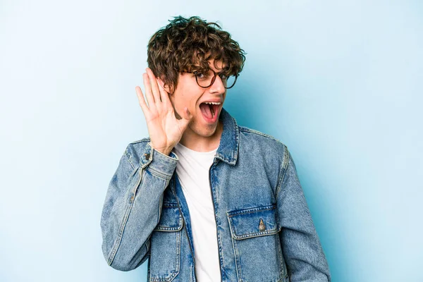 Mavi arka planda izole edilmiş genç beyaz adam bir dedikoduyu dinlemeye çalışıyor..