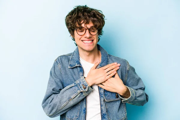Mavi arka planda izole edilmiş beyaz bir genç, dost bir ifadeye sahip, avuçlarını göğsüne bastırıyor. Aşk konsepti.