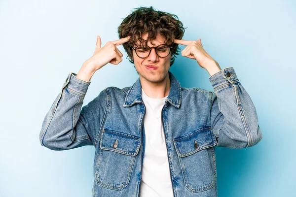 Kafkasyalı genç adam mavi arka planda izole edilmiş bir göreve odaklanmış, parmaklarını işaret ediyor..