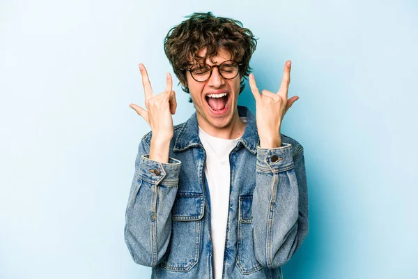 Mavi arka planda izole edilmiş genç beyaz adam boynuzlarını devrim konsepti olarak gösteriyor..