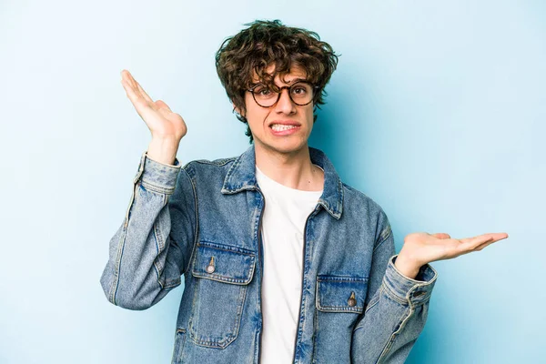 Kafkasyalı genç adam mavi arka planda izole edilmiş. Kafası karışmış ve omuz silkiyor. Kopya alanını tutmak için..