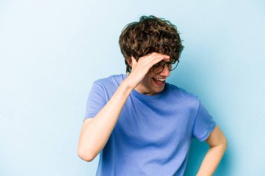 Kafkasyalı genç adam mavi arka planda izole edilmiş neşeli bir şekilde gülüyor. Mutluluk kavramı.