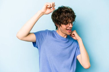 Mavi arka planda izole genç beyaz adam özel bir günü kutluyor, atlıyor ve enerjiyle kollarını kaldırıyor..