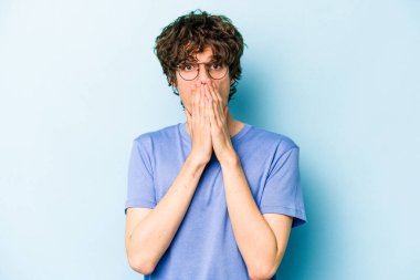Kafkasyalı genç adam mavi arka planda izole edilmiş ağzı kapalı ve elleri endişeli görünüyor..