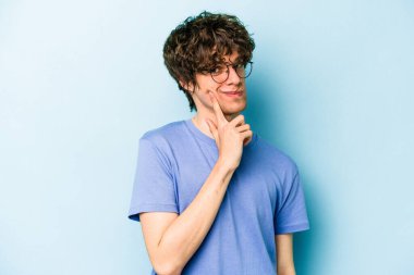 Kafkasyalı genç bir adam mavi arka planda izole edilmiş. Bir strateji planlıyor, bir iş yolu düşünüyor..