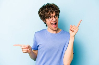 Mavi arka planda izole edilmiş genç beyaz adam farklı kopya alanlarını gösteriyor, birini seçiyor, parmaklarıyla gösteriyor.