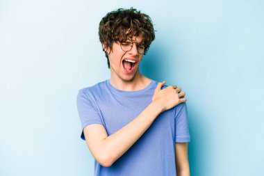 Mavi arka planda izole edilmiş, omuz ağrısı olan genç beyaz bir adam..