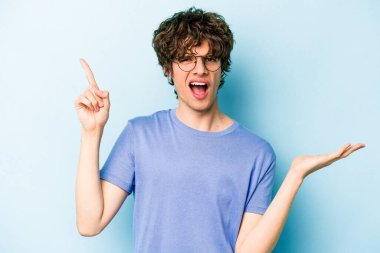 Kafkasyalı genç adam mavi arka planda izole edilmiş ve elinde bir ürün tutuyor..