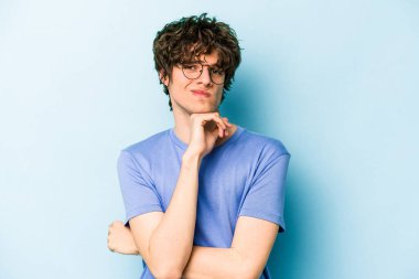 Kafkasyalı genç adam mavi arka planda izole edilmiş düşünüyor ve bakıyor, yansıtıyor, düşünüyor, bir fantezi kuruyor..