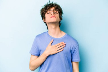 Kafkasyalı genç adam mavi arka planda izole edilmiş yemin ediyor, elini göğsüne koyuyor..