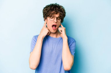 Genç beyaz adam mavi arka planda izole edilmiş parmaklarıyla kulaklarını kapatıyor, gürültülü bir ortam tarafından stresli ve umutsuz..