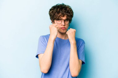 Kafkasyalı genç bir adam mavi arka planda izole edilmiş. Yumruk atıyor, sinirleniyor, kavga ediyor, kavga ediyor..