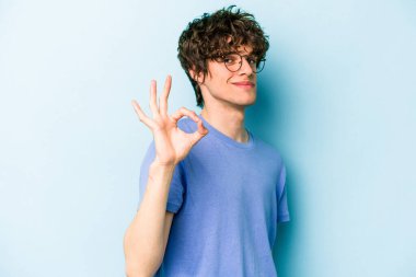 Kafkasyalı genç bir adam mavi arka planda izole edilmiş bir şekilde göz açıp kapayana kadar iyi bir el hareketi yapıyor..