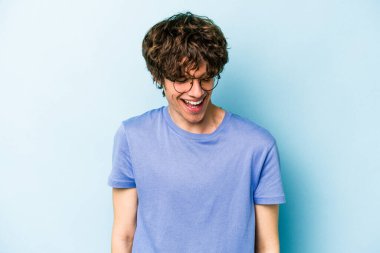 Mavi arka planda izole edilmiş genç beyaz adam gülüyor ve gözlerini kapıyor, rahatlamış ve mutlu hissediyor..
