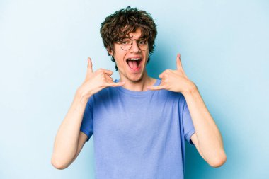 Mavi arka planda izole edilmiş genç beyaz adam parmaklarıyla bir cep telefonu hareketi gösteriyor..