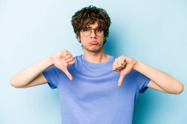 Mavi arka planda izole edilmiş genç beyaz bir adam hoşlanmadığı bir jest yapıyor. Anlaşmazlık konsepti.