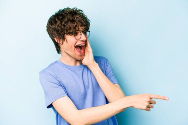 Kafkasyalı genç adam mavi arka planda izole edilmiş. Dedikodu yapıyor, bir şeyleri bildiriyor..