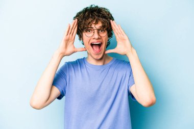 Mavi arka planda izole edilmiş genç beyaz adam hoş bir sürpriz alıyor, heyecanlı ve el kaldırıyor..