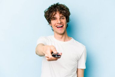 Elinde televizyon kumandası olan beyaz bir adam mavi arka planda izole edilmiş.