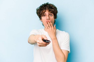 Elinde televizyon kumandası olan beyaz bir adam mavi arka planda izole edilmiş.