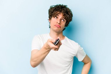 Elinde televizyon kumandası olan beyaz bir adam mavi arka planda izole edilmiş.