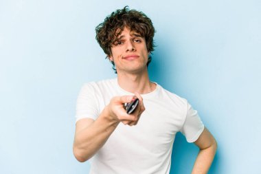 Elinde televizyon kumandası olan beyaz bir adam mavi arka planda izole edilmiş.