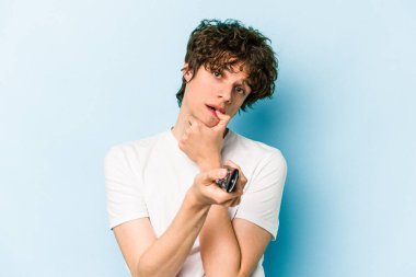 Elinde televizyon kumandası olan beyaz bir adam mavi arka planda izole edilmiş.