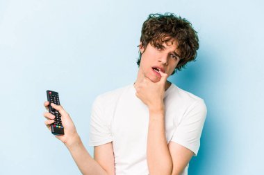 Elinde televizyon kumandası olan beyaz bir adam mavi arka planda izole edilmiş.