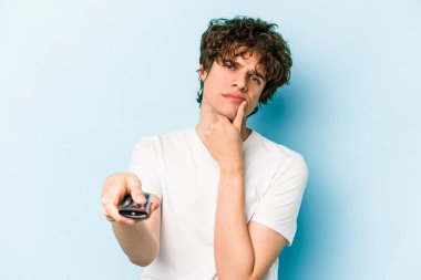 Elinde televizyon kumandası olan beyaz bir adam mavi arka planda izole edilmiş.