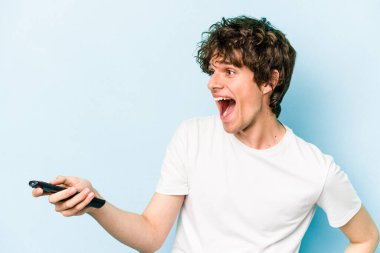Elinde televizyon kumandası olan beyaz bir adam mavi arka planda izole edilmiş.