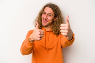 Beyaz arka planda izole edilmiş genç beyaz bir adam iki parmağını da kaldırıyor, gülümsüyor ve kendinden emin..