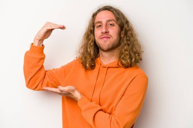 Beyaz arka planda izole edilmiş genç beyaz bir adam işaret parmaklarıyla küçük bir şey tutuyor, gülümsüyor ve kendinden emin..