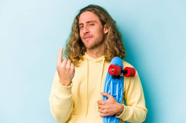 Genç kaykaycı beyaz adam mavi arka planda izole edilmiş. Sanki seni davet ediyormuş gibi parmağıyla işaret ediyor..