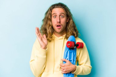 Genç kaykaycı beyaz adam mavi arka planda izole edildi. Şaşırdı ve şok oldu..