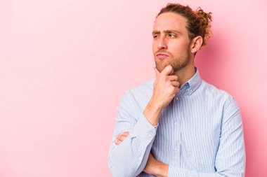 Pembe arka planda izole edilmiş genç beyaz adam şüpheli ve şüpheci bir ifadeyle yana bakıyor..