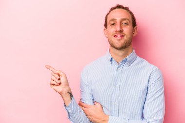 Pembe arka planda izole edilmiş genç beyaz adam işaret parmağıyla işaret ederek gülümsüyor..