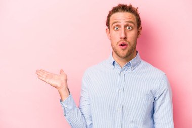 Pembe arka planda izole edilmiş genç beyaz adam, avuç içi fotokopi alanını elinde tutmaktan etkilenmiş..