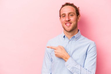 Pembe arka planda izole edilmiş genç beyaz adam gülümsüyor ve boş alanda bir şeyler gösteriyor..