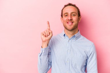 Pembe arka planda izole edilmiş genç beyaz bir adam bir numarayı parmağıyla gösteriyor..