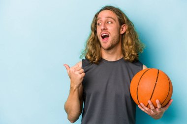Basketbol oynayan beyaz bir genç, mavi arka planda soyutlanmış, baş parmak uzakta, gülen ve kaygısız..