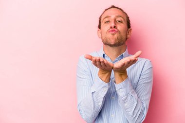Genç beyaz adam pembe arka planda izole edilmiş dudaklar kıvrılmış ve hava öpücüğü göndermek için avuç içleri tutulmuş..